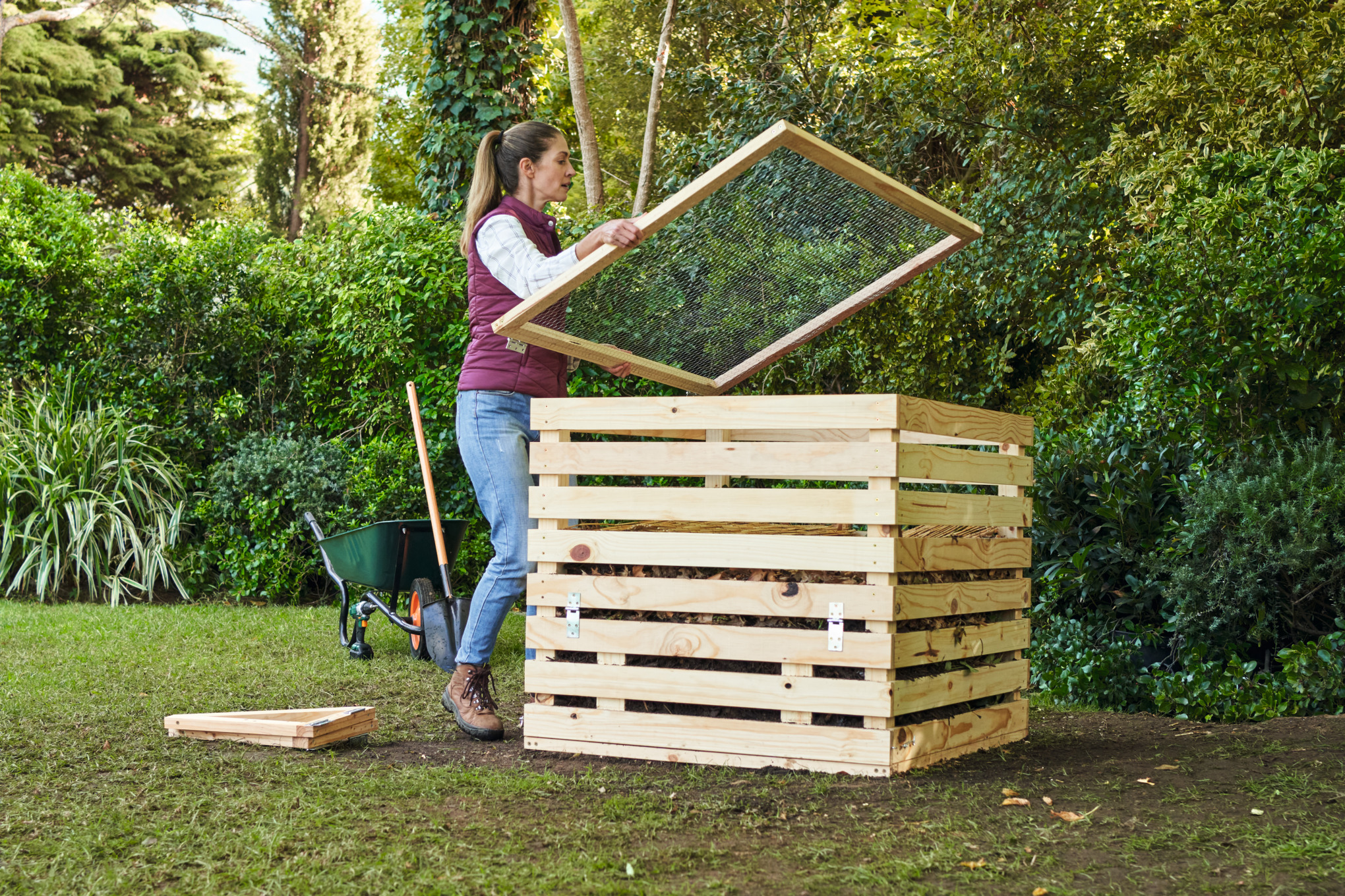 Uma mulher num canto do jardim a tapar uma composteira de bricolage