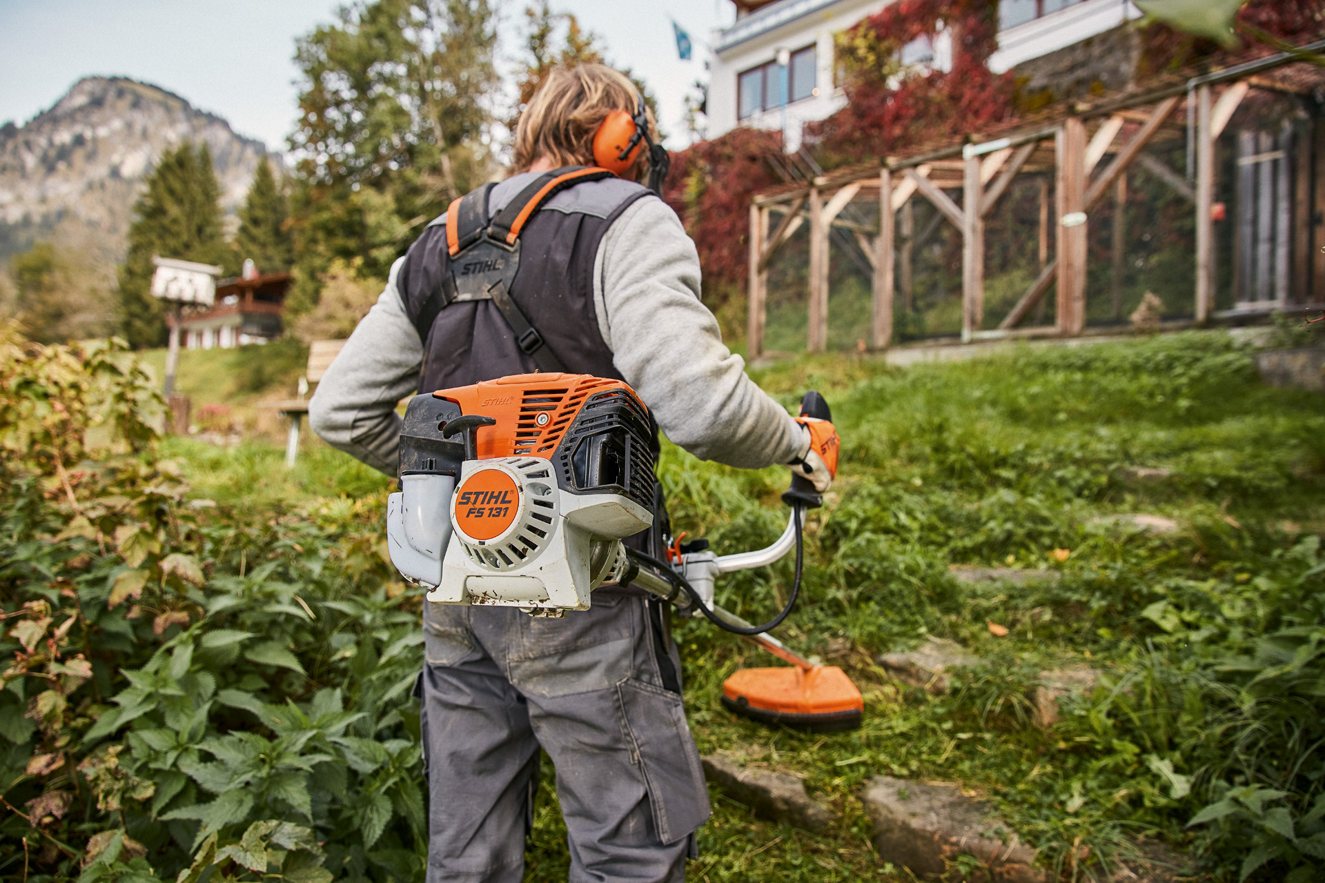 Pessoa usa uma rpçadeira com motor STIHL 4-MIX® FS 131 a gasolina em terreno relvado irregular à frente de uma casa