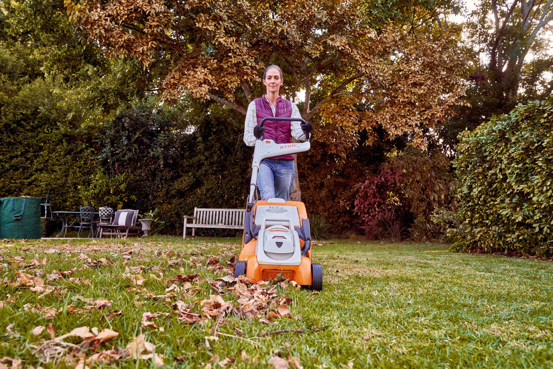 Mulher aplica os cuidados com a grama no outono ao usar um cortador de grama a bateria STIHL RMA 339 C num espaço verde