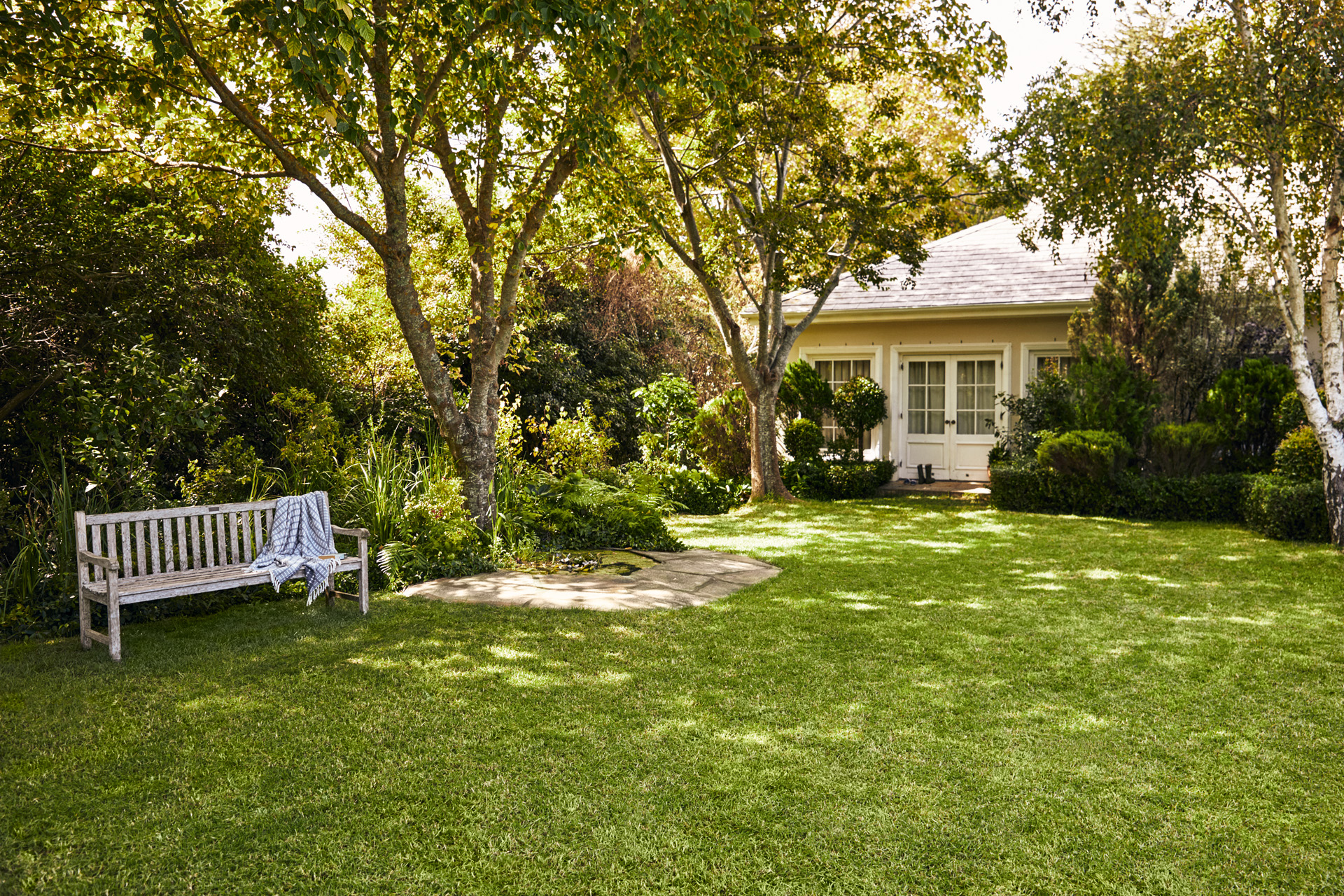 Pequena casa com espaço verde; em primeiro plano, um banco de jardim sobre gramado verde