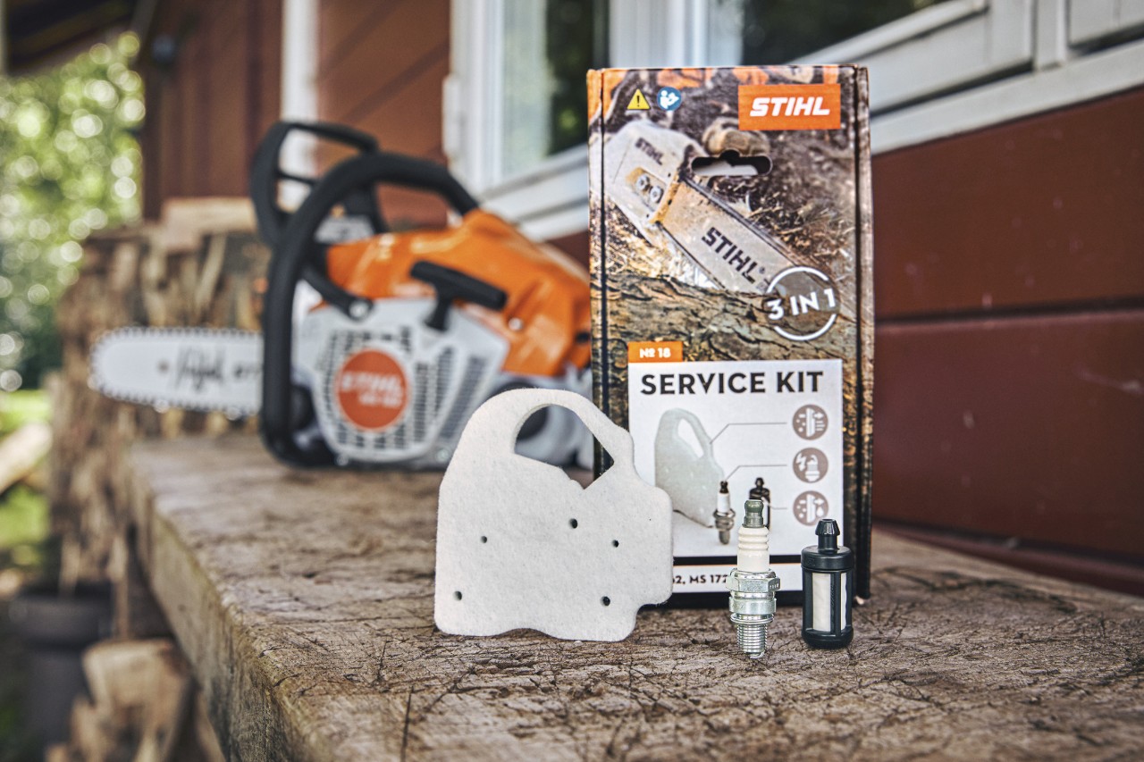 Kit de manutenção STIHL 18 numa bancada de trabalho, à frente dos componentes individuais filtro de ar de velo, vela de ignição e filtro de combustível