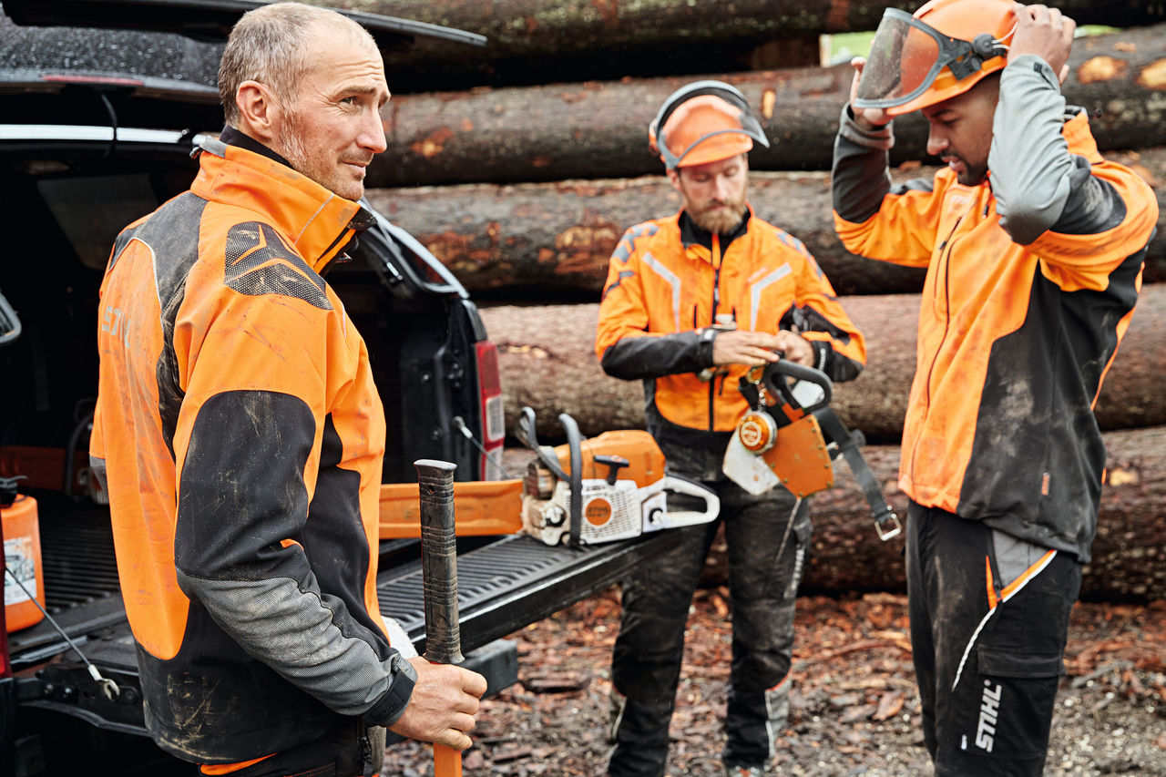 Três homens com equipamento de proteção STIHL junto a um veículo com mala aberta