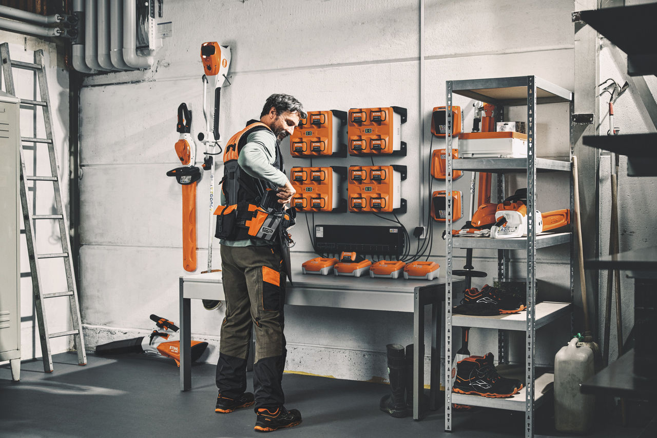 Um homem num armazém com máquinas e baterias STIHL a usar o sistema de arnês modular STIHL ADVANCE X-Flex 